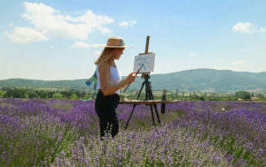 Celeste painting in lavender field. Paintbrush in hand. Provence